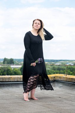 Yemyeşil vücut şekilleri uzun elbiseli bir genç kadınla bir binanın çatı üzerinde dans ediyor