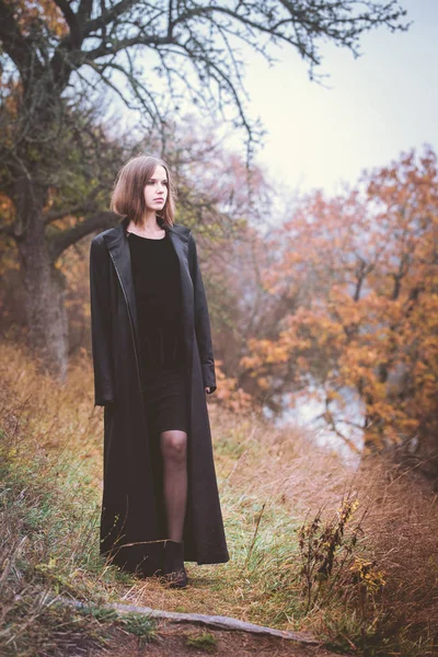 在河上的悬崖上穿黑色长外套的女人 — 图库照片