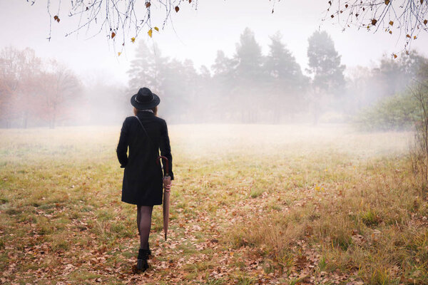 Женщина в черном пальто и шляпе в туманную погоду

