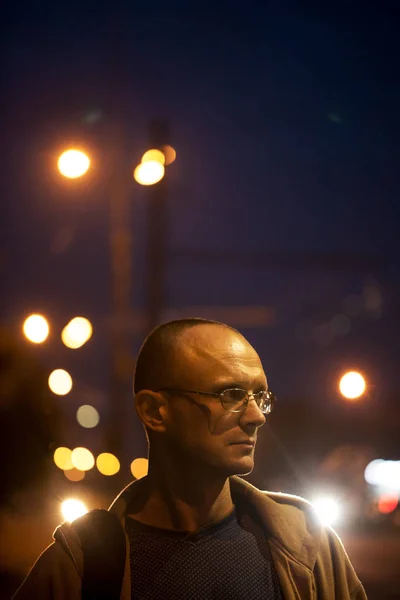 A young man with glasses on the background of the lights of the night city