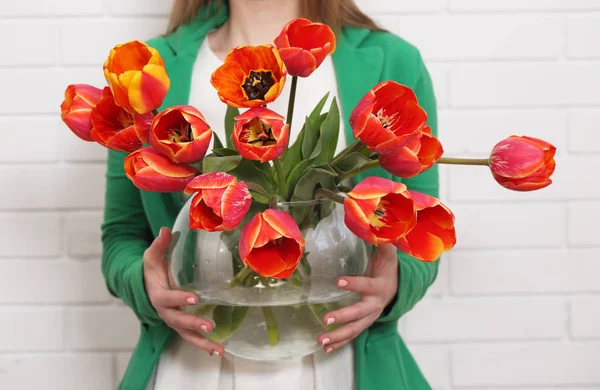 woman holds a vase with a large bouquet of tulips.