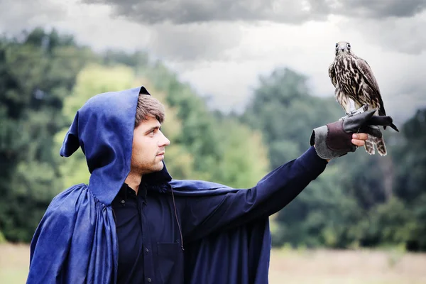 英俊的年轻男子在一件雨衣和一只猎鹰在他的手 — 图库照片