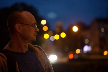 Gece şehir ışıkları arka planda gözlüklü genç bir adam
