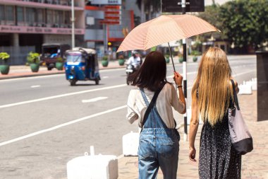 İki kız sıcak bir günde bir şemsiye altında yürüyor