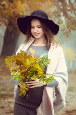 Şapkalı güzel bir kız sonbahar ormanın üzerinde yürüyor