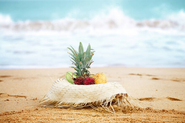 Exotic fruits in a straw hat near the ocean