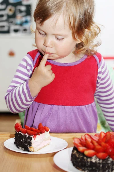 The little blue-eyed girl eating cake with strawberries