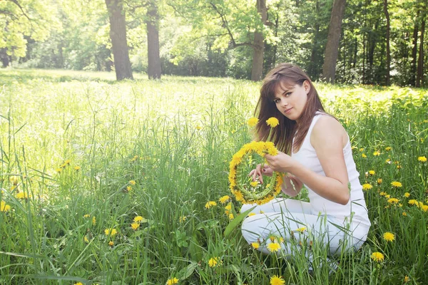 美しい若い女性はタンポポの花輪を編む — ストック写真