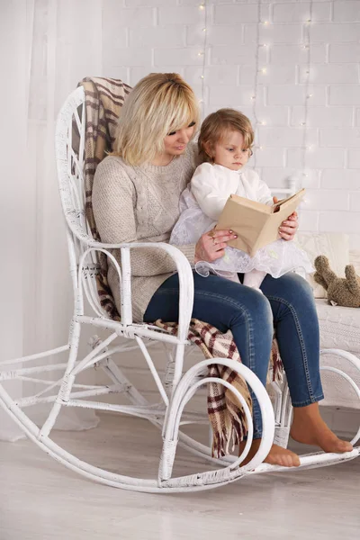 籐の椅子に座っている娘に本を読んでママ — ストック写真
