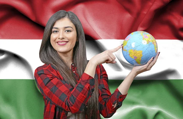 Young female Tourist holding Earth Globe against flag of Hungary
