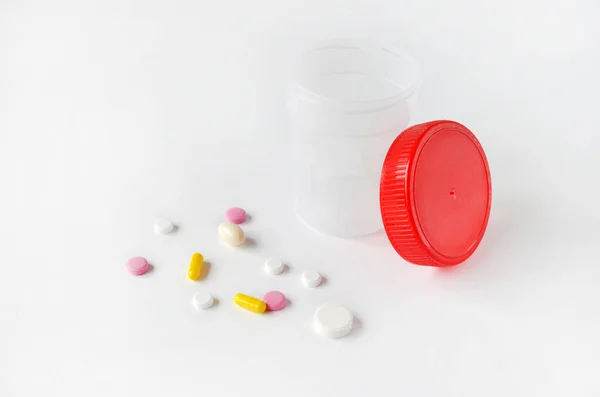 Multicolored pills and clear plastic urine container on white background