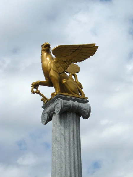 在多云的天空背景上 在柱子上有一把钥匙的金狮鹫 — 图库照片