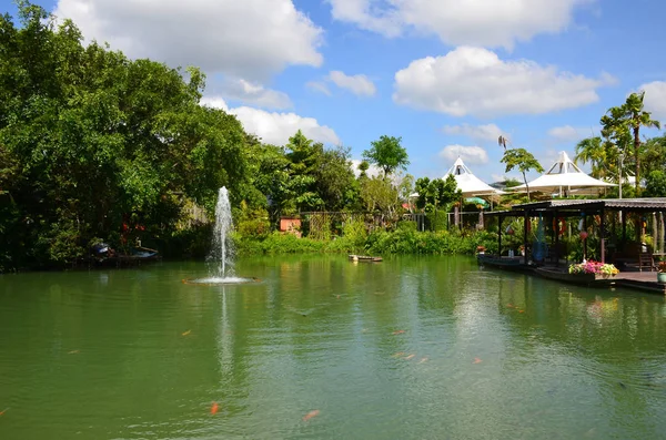 Manzara kırmızı carps ve yeşil ağaçlar güneşli bir arka plan üzerinde bir çeşme ile yeşil bir gölet. Gölet yakınındaki Arbors