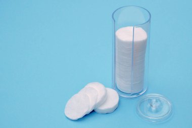 Pamuk tamponlarla parlak mavi arka plan ile bir kapak ile açık şeffaf plastik şişe. Pamuk pedler yalan dışında