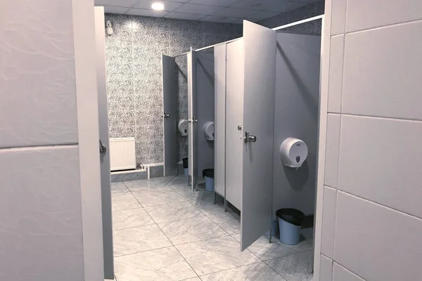 一个敞开大门的公共厕所的内部以灰色的色调摆摊 人造照明 地板上的灰色瓷砖 垃圾桶 卫生纸架 侧视图 — 图库照片