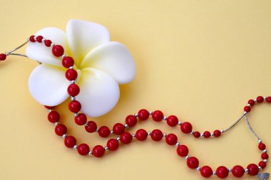 White with yellow flower and bright red coral beads with silver accents on a yellow background. Concept of International Women's Day, Mother's Day, Valentine's Day