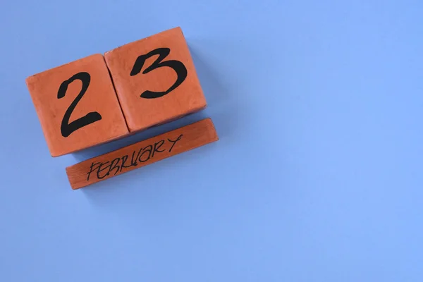 Perpetual wooden calendar with the date of February 23 in the corner on a blue background with copy space. Concept of holiday, Defender of the Fatherland Day, courage, strength. Horizontal photo