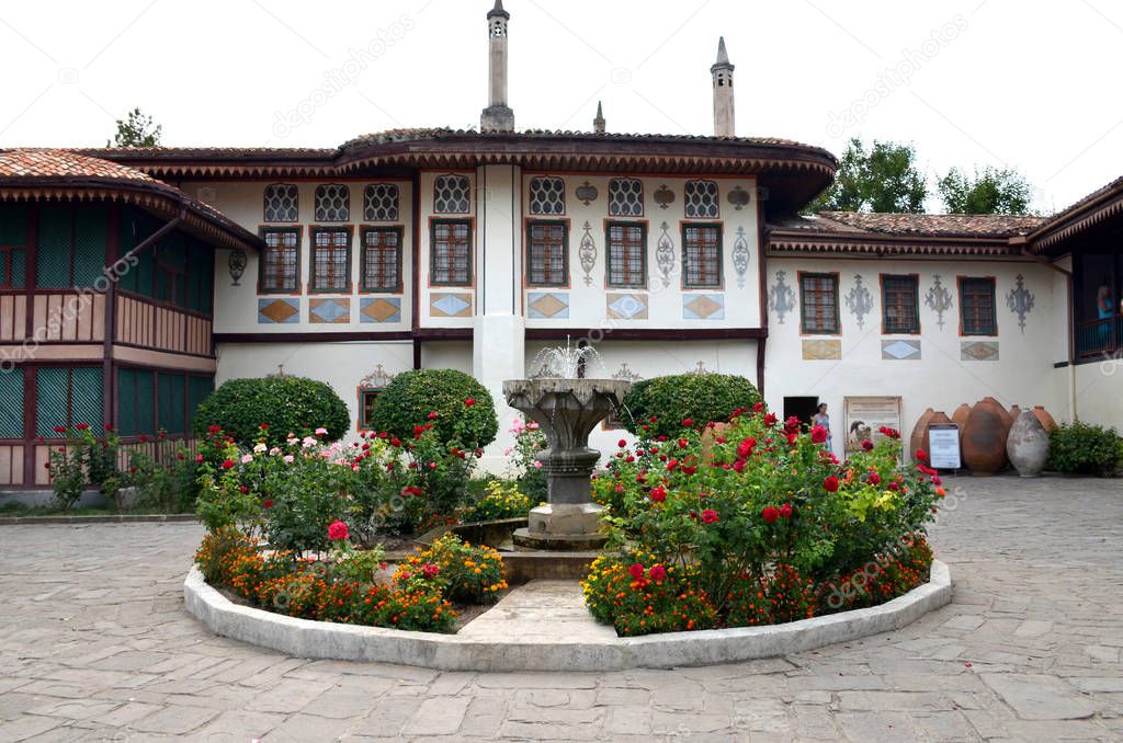 Courtyard of the Khans Palace in Bakhchisarai, Crimea, Russia. Decorative stone fountain surrounded by rose bushes and other flowers