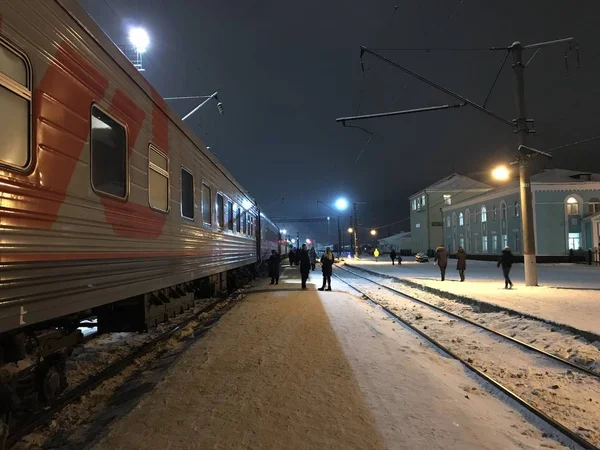 Cherepovets, Russia - December 28, 2018: A stop of long-distance train on a winter snowy evening under light of lanterns. Travel with the company Russian Railways. People went out into the fresh air.