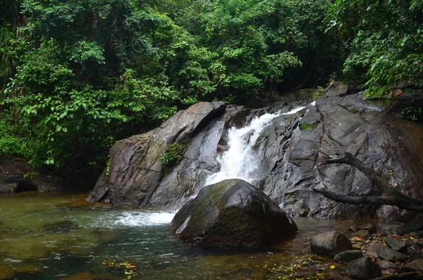 Une petite cascade tombe d'une falaise de pierre dans un lac entourant — Photo