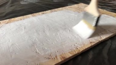 Siyah bir arka planda beyaz OSB panelinden ahşap bir raf boyama süreci. Beyaz boya ile düz ahşap boya fırçası yakın çekim