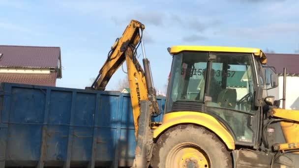 俄罗斯圣彼得堡 2019年4月20日 一辆黄色大拖拉机将建筑垃圾装入装有水桶的容器中 然后按压 在山寨村领土上的垃圾收集 — 图库视频影像
