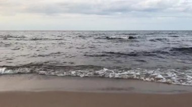 Göl kıyısı kasvetli bulutlu bir gün. Dalgalar kumlu kıyıda yuvarlanıyor. Yan görünüm