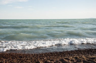 Deniz sahilinde çakıl taşları, köpüklü dalgalar.