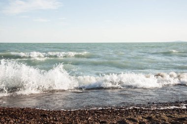 Deniz sahilinde çakıl taşları, köpüklü dalgalar.