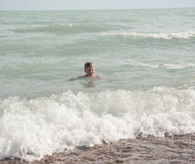 Genç çocuk sahilde dalgalar ile eğleniyor