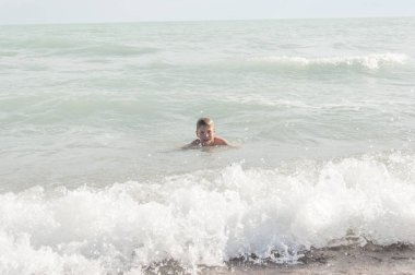 Genç çocuk sahilde dalgalar ile eğleniyor