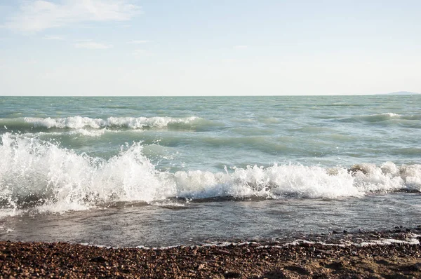 Deniz sahilinde çakıl taşları, köpüklü dalgalar.