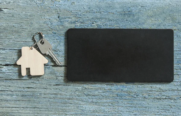テキストの黒の基板上の木製の背景に銀の鍵と家の平面図記号を宣伝または製品 — ストック写真