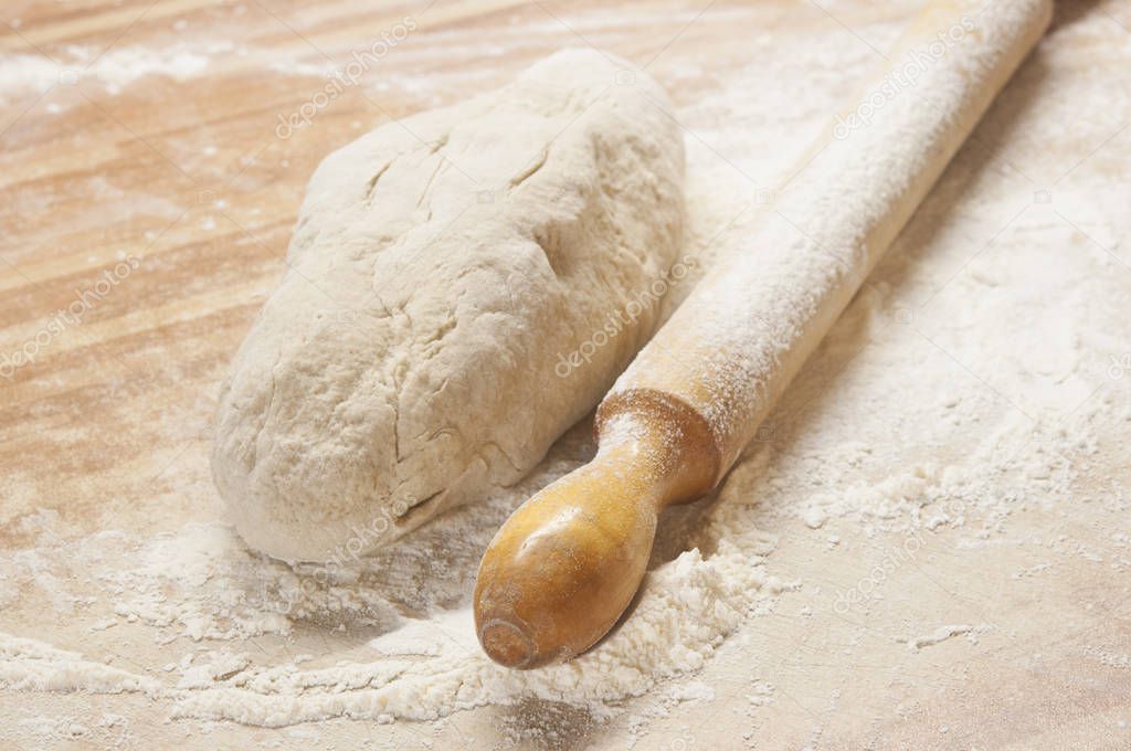yeasty dough and rolling pin on wooden surface