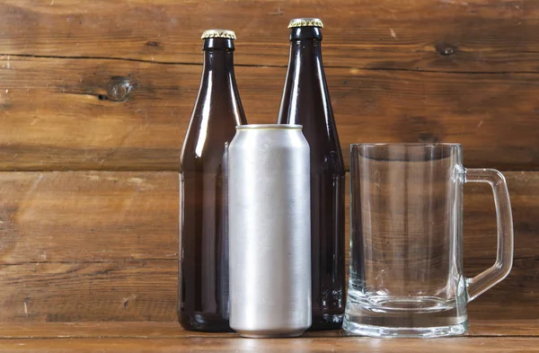 blank metallic can and glass bottle of beer on a wooden background