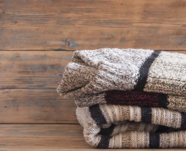 Ahşap arka planda örülmüş kış kıyafetleri, kazaklar, örgü giysileri, metin için yer.