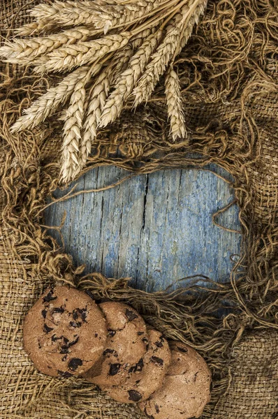 Agricultural still life from ears of wheat and chocolate cookies on a wood background. Top view