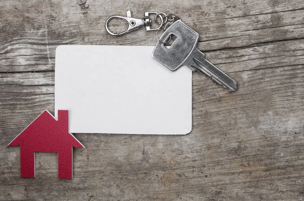 Silver key and blank business card on wooden background. Real estate concept.