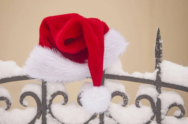 圣诞老人的帽子在老式的钉栅栏对着黄色的墙壁 一些雪 圣诞节庆祝概念 — 图库照片
