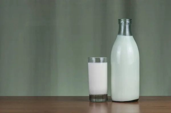 A bottle of milk and glass mug of milk with light green background