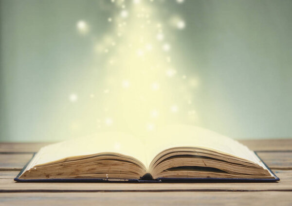 Old open book with magic light and falling stars on wood planks and dark abstract background