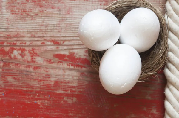 White eggs in easter nest on wood background.