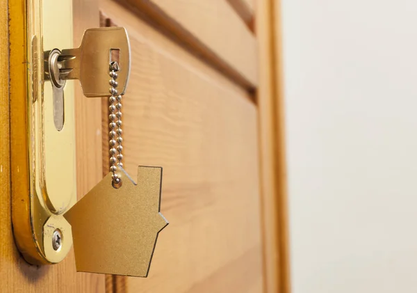 Porte-clés de la maison sur un porte-clés en argent en forme de maison dans la serrure d'une porte — Photo