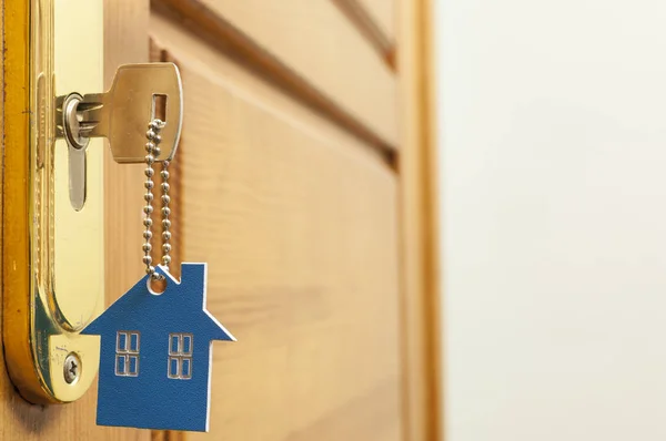 Llave de la casa en un llavero de plata en forma de casa en la cerradura de una puerta —  Fotos de Stock