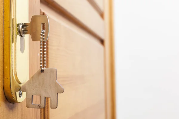 House key on a house shaped silver keyring in the lock of a door — Stock Photo, Image