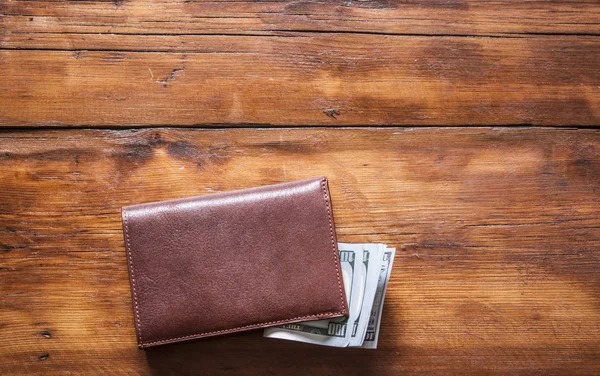 Кожаный бумажник на деревянном столе с долларовыми купюрами — стоковое фото
