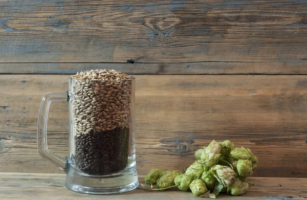 Tasse en verre de grain et houblon sur une vieille table en bois . — Photo