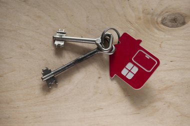 Ahşap arka planda ev şeklindeki anahtarlığın anahtarı. Gerçek 