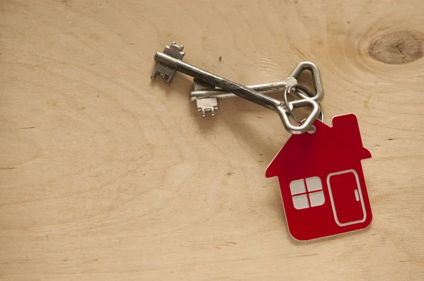 Klucz do domu na breloczku w kształcie domu na drewnianym tle. Prawdziwe. — Zdjęcie stockowe
