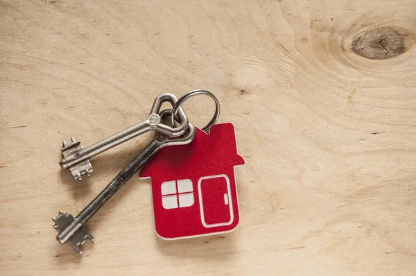 House key on a house shaped keychain on wooden background. Real — Stock Photo, Image
